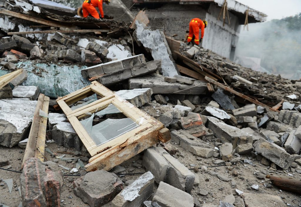 Men in orange jumpsuits searching through the wreckage ofa  destroyed home